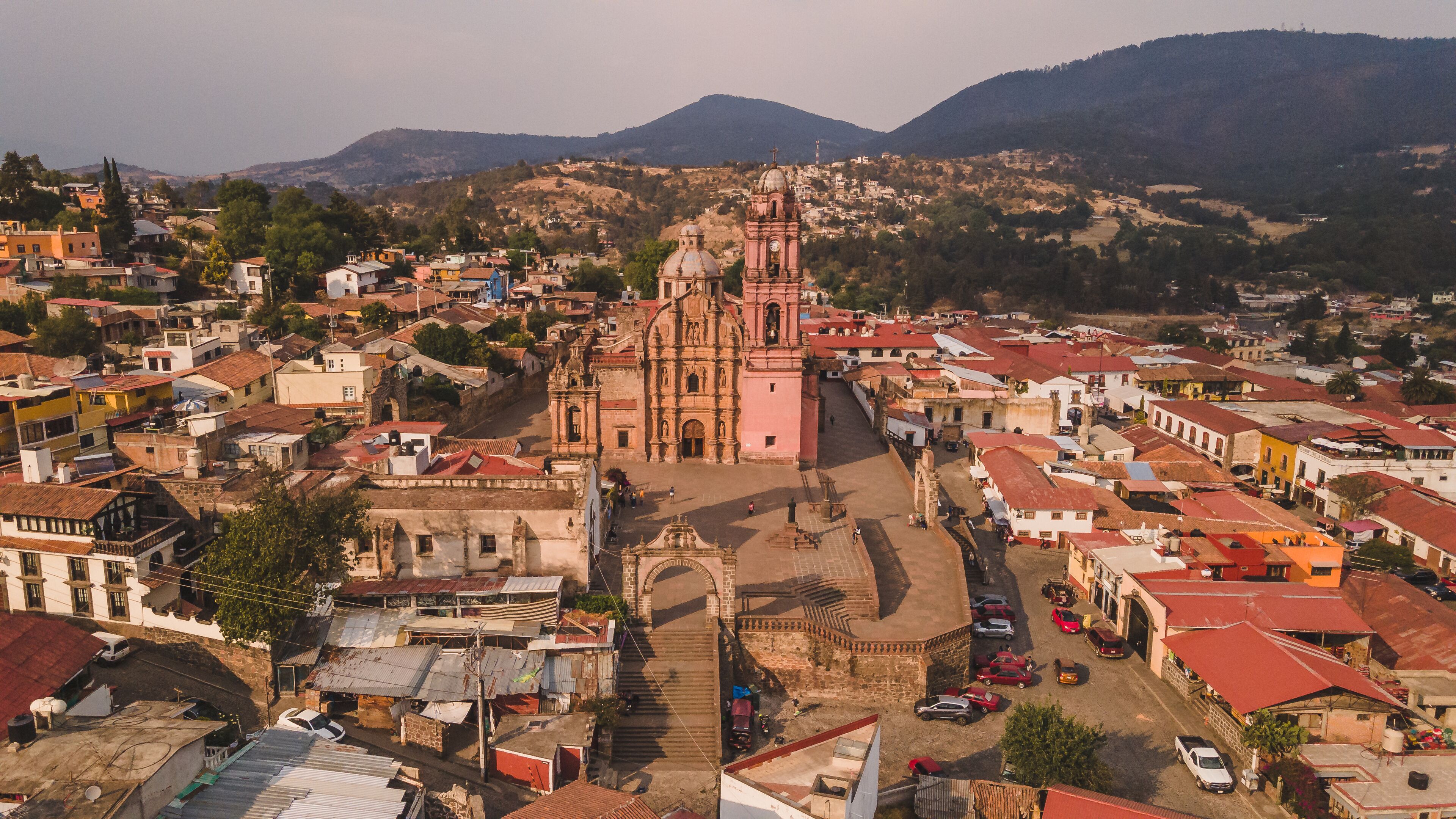 A historic town with a prominent pink church, cobblestone streets, and surrounding hills.