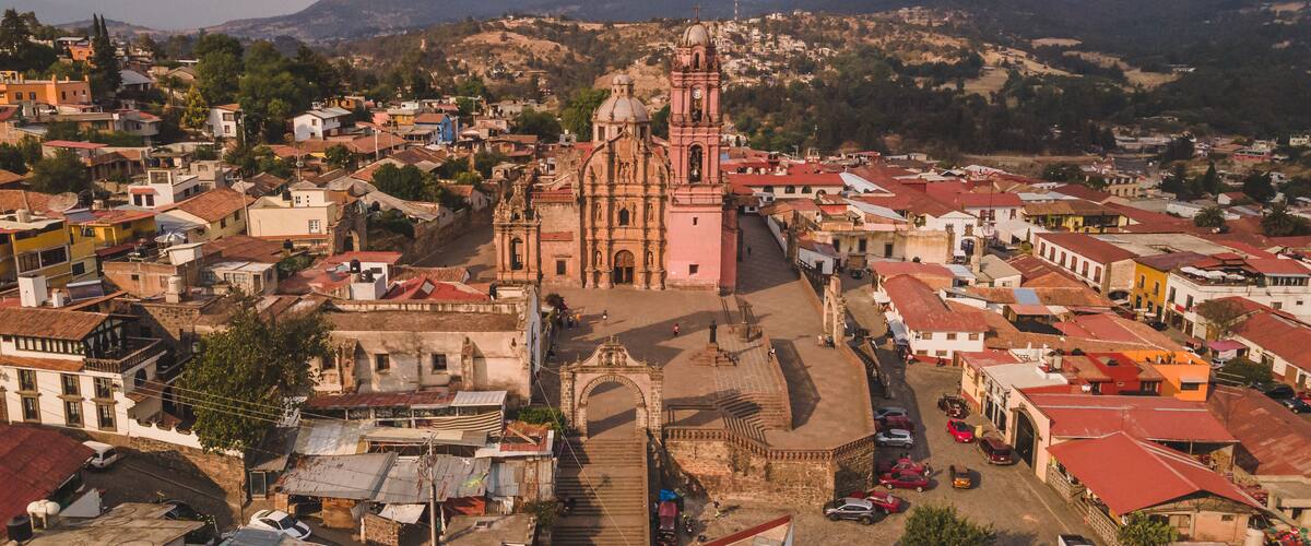 A historic town with a prominent pink church, cobblestone streets, and surrounding hills.