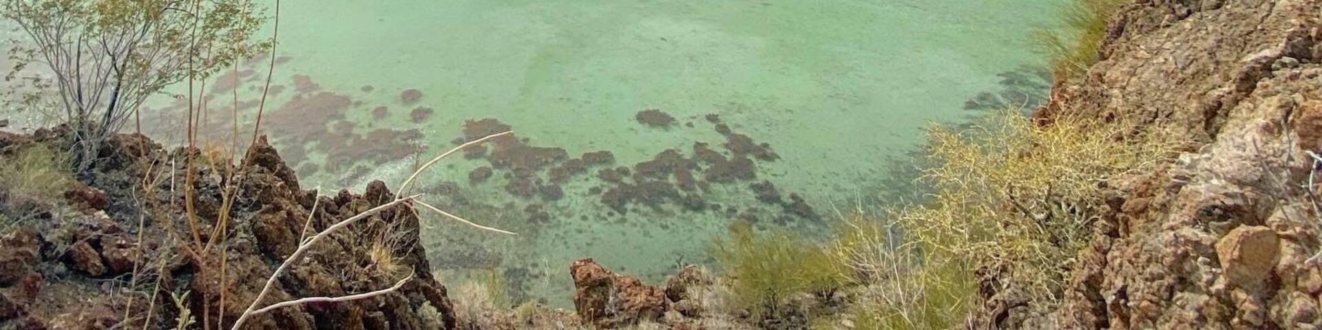 Un paysage côtier caractérisé par une eau turquoise cristalline, des bateaux et un arrière-plan montagneux.