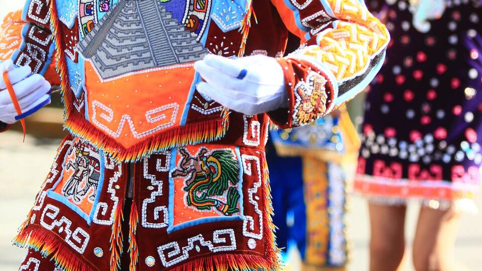 A person in a colorful traditional costume with intricate patterns and a large headdress.