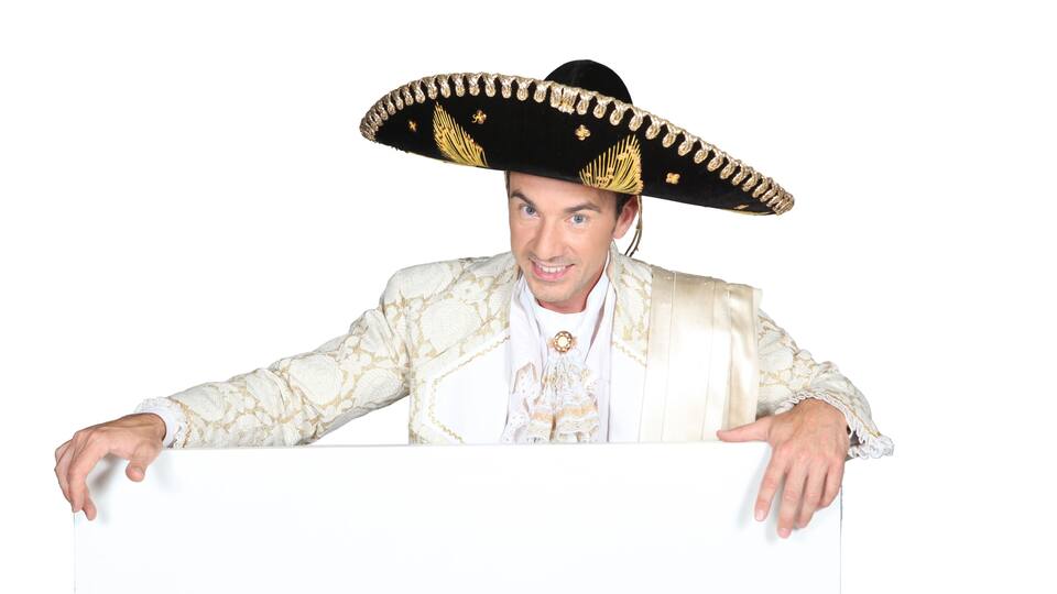 A person wearing a large black sombrero with gold embroidery and a white and gold patterned jacket.