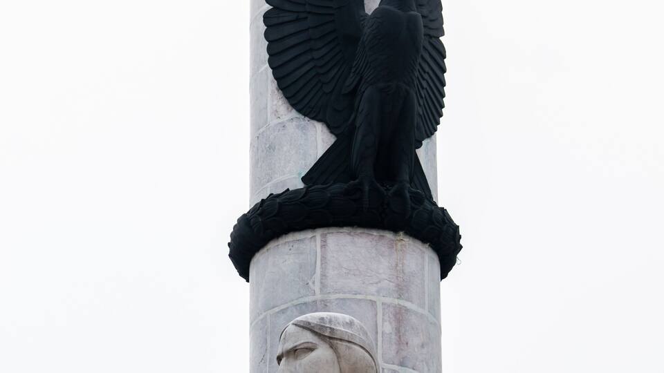A statue of a winged figure atop a column with a seated figure below.
