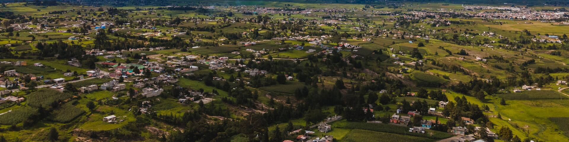 A panoramic view of a town surrounded by green fields and mountains in the distance.