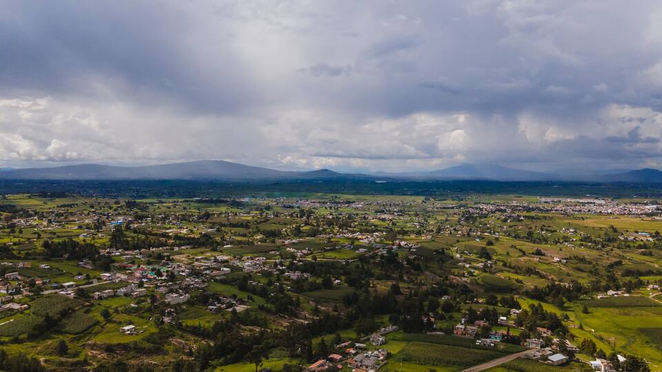 A panoramic view of a town surrounded by green fields and mountains in the distance.