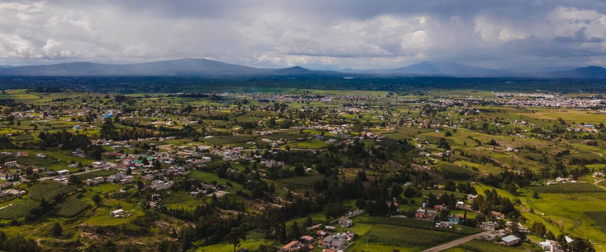 A panoramic view of a town surrounded by green fields and mountains in the distance.