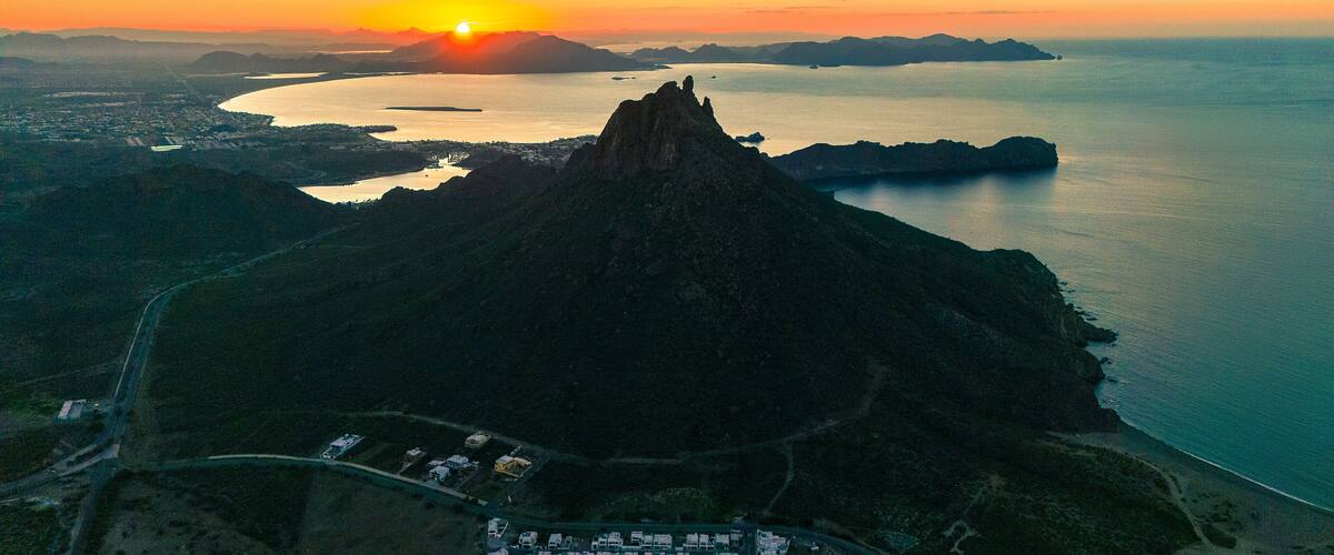 A mountain with a peak, a body of water, and a distant sun.