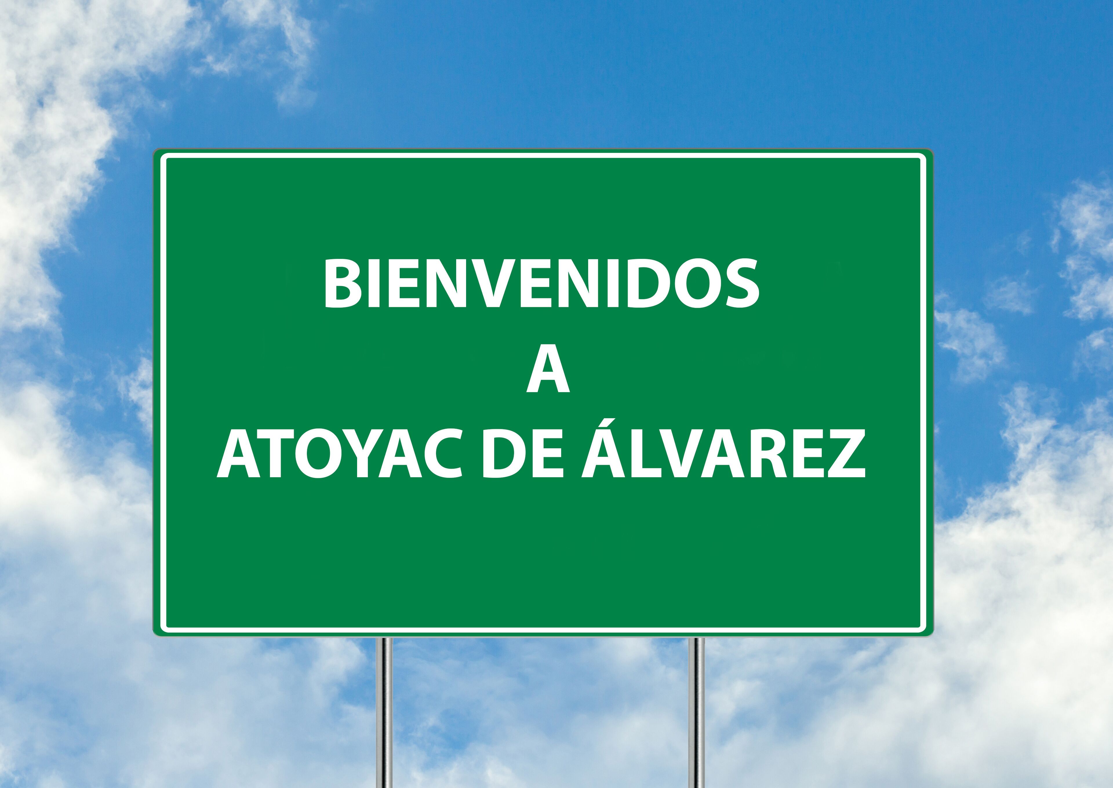 A green welcome sign with the text "BIENVENIDOS A ATOYAC DE ÁLVAREZ" against a blue sky with clouds.