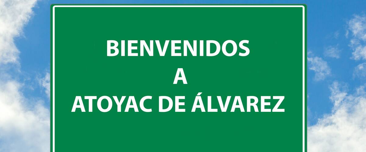 A green welcome sign with the text "BIENVENIDOS A ATOYAC DE ÁLVAREZ" against a blue sky with clouds.
