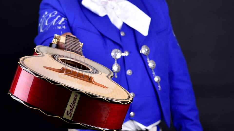 A person in a blue suit holding a guitar and wearing a large sombrero.