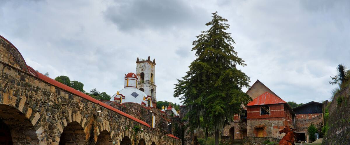 A historic stone building with arches, a church with a bell tower, and a statue of a horse.