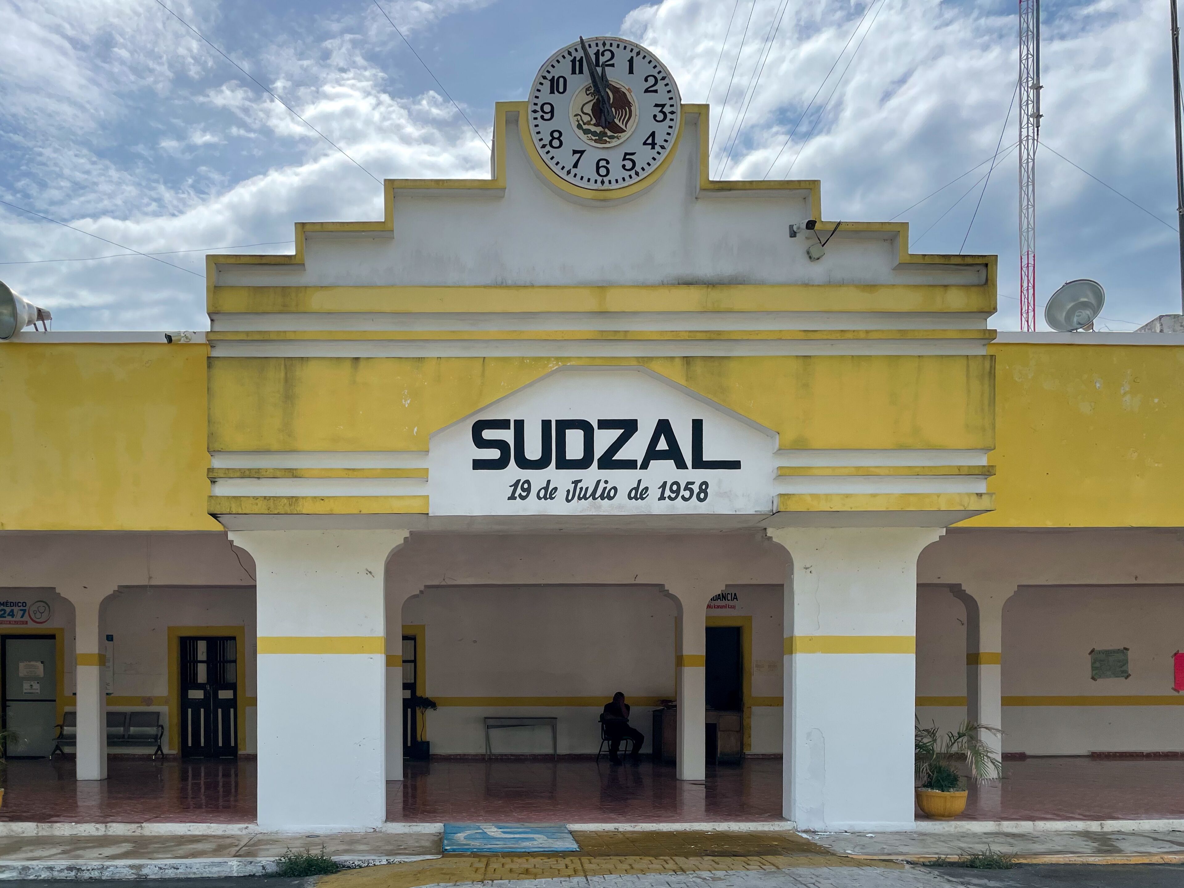 A building with a clock and a sign reading 'SUDZAL 19 de Julio de 1958'.