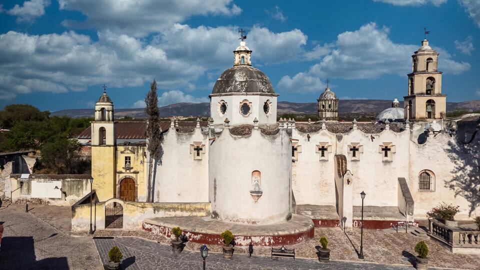 A historic church with a prominent dome and bell towers, set against a mountainous backdrop.