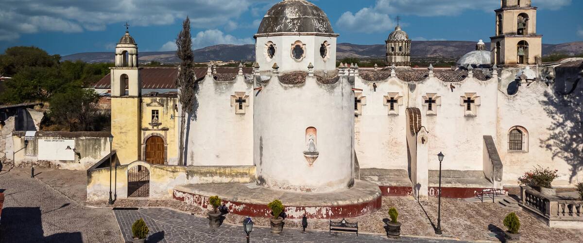 A historic church with a prominent dome and bell towers, set against a mountainous backdrop.