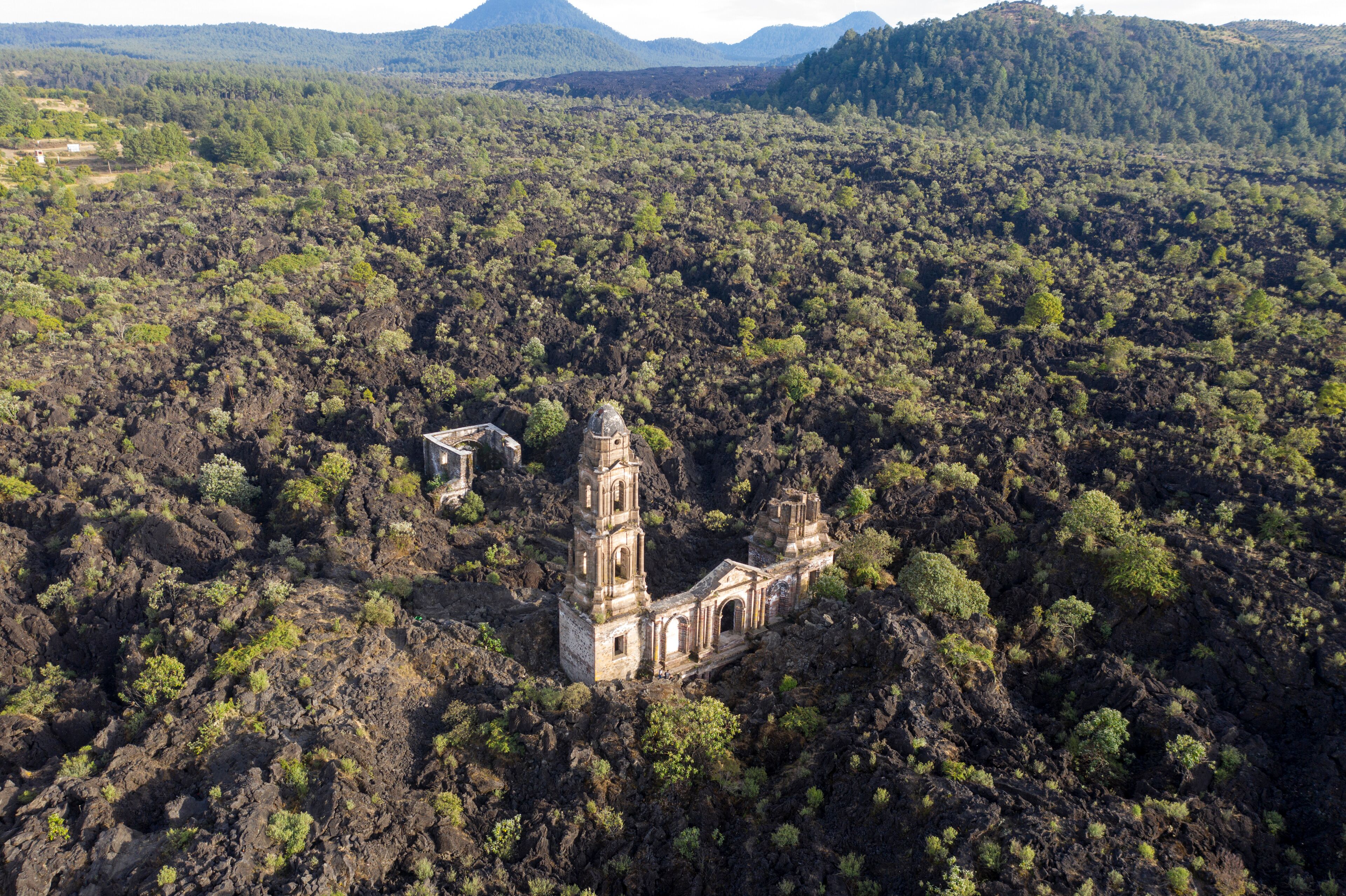 An abandoned church surrounded by dense forest and mountains.