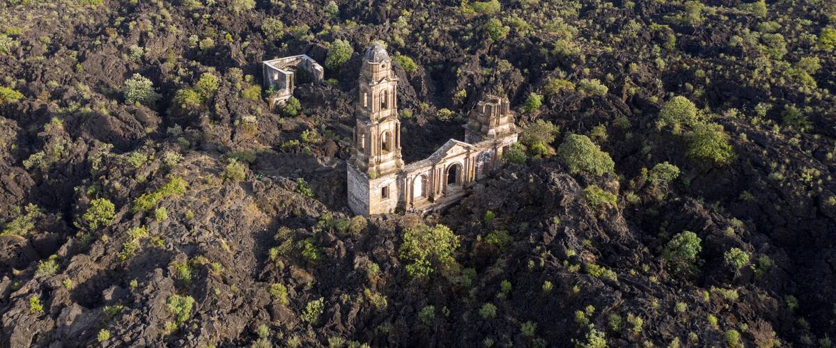 An abandoned church surrounded by dense forest and mountains.