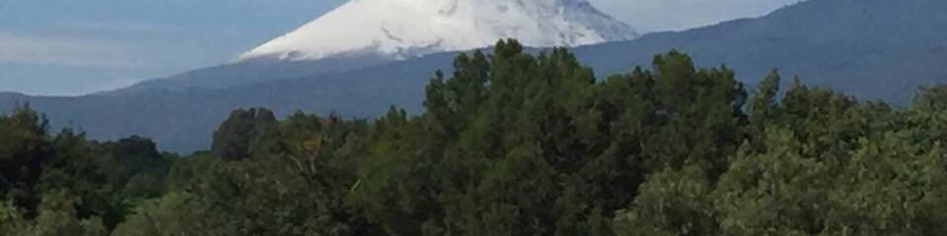 A snow-capped mountain with a plume of smoke rising from its peak.