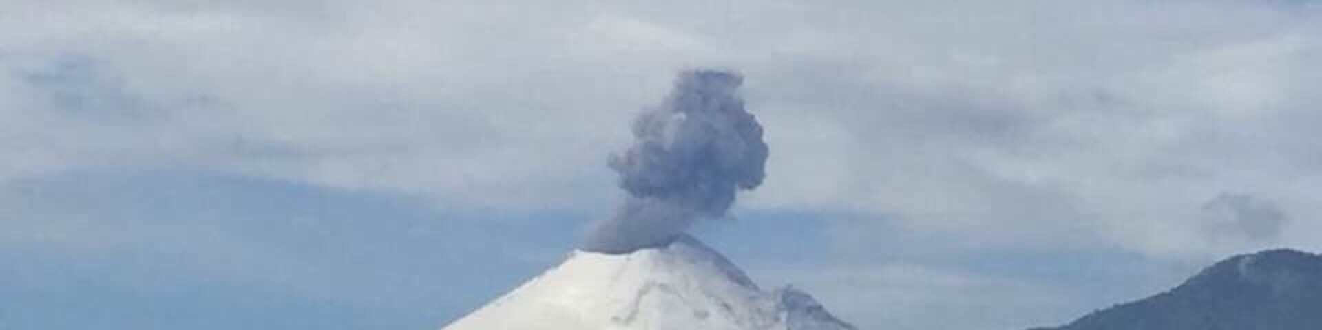Una montaña nevada con una columna de humo elevándose de su cima.