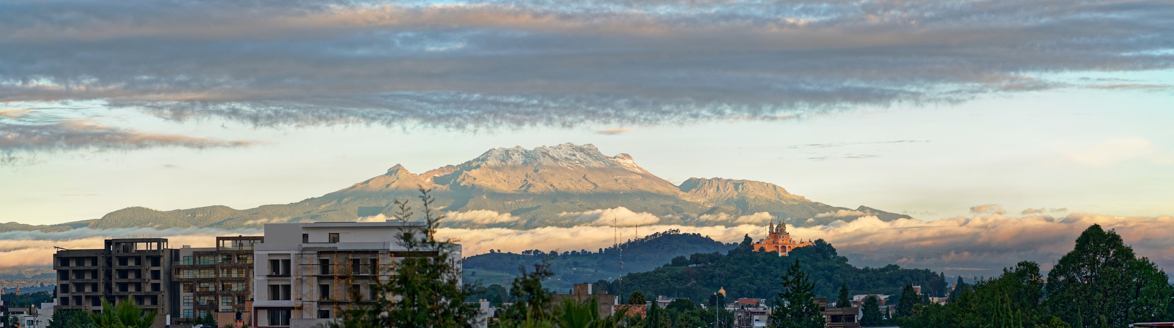 A mountain range with a prominent peak, a temple-like structure on a hill, and modern buildings in the foreground.