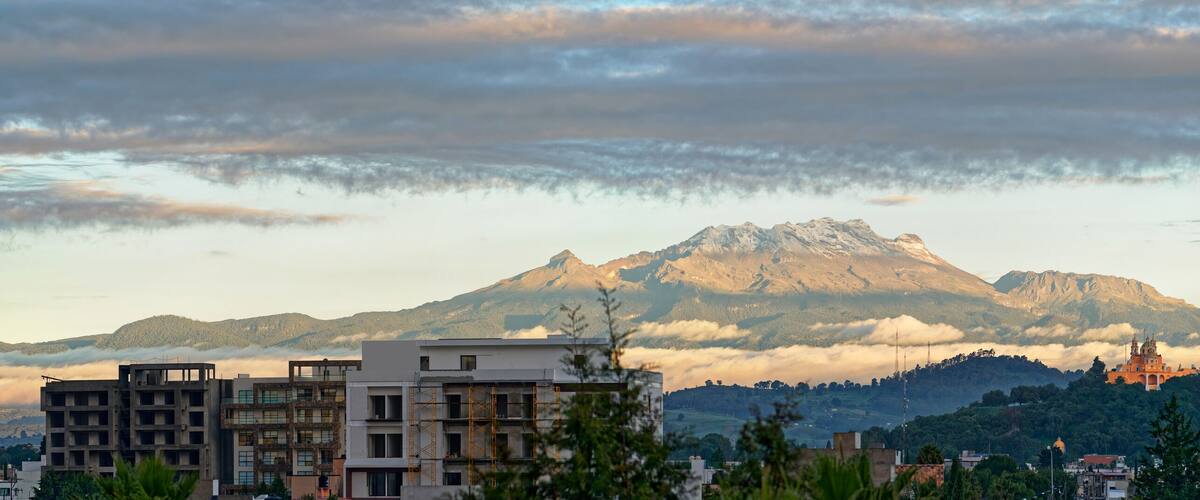A mountain range with a prominent peak, a temple-like structure on a hill, and modern buildings in the foreground.