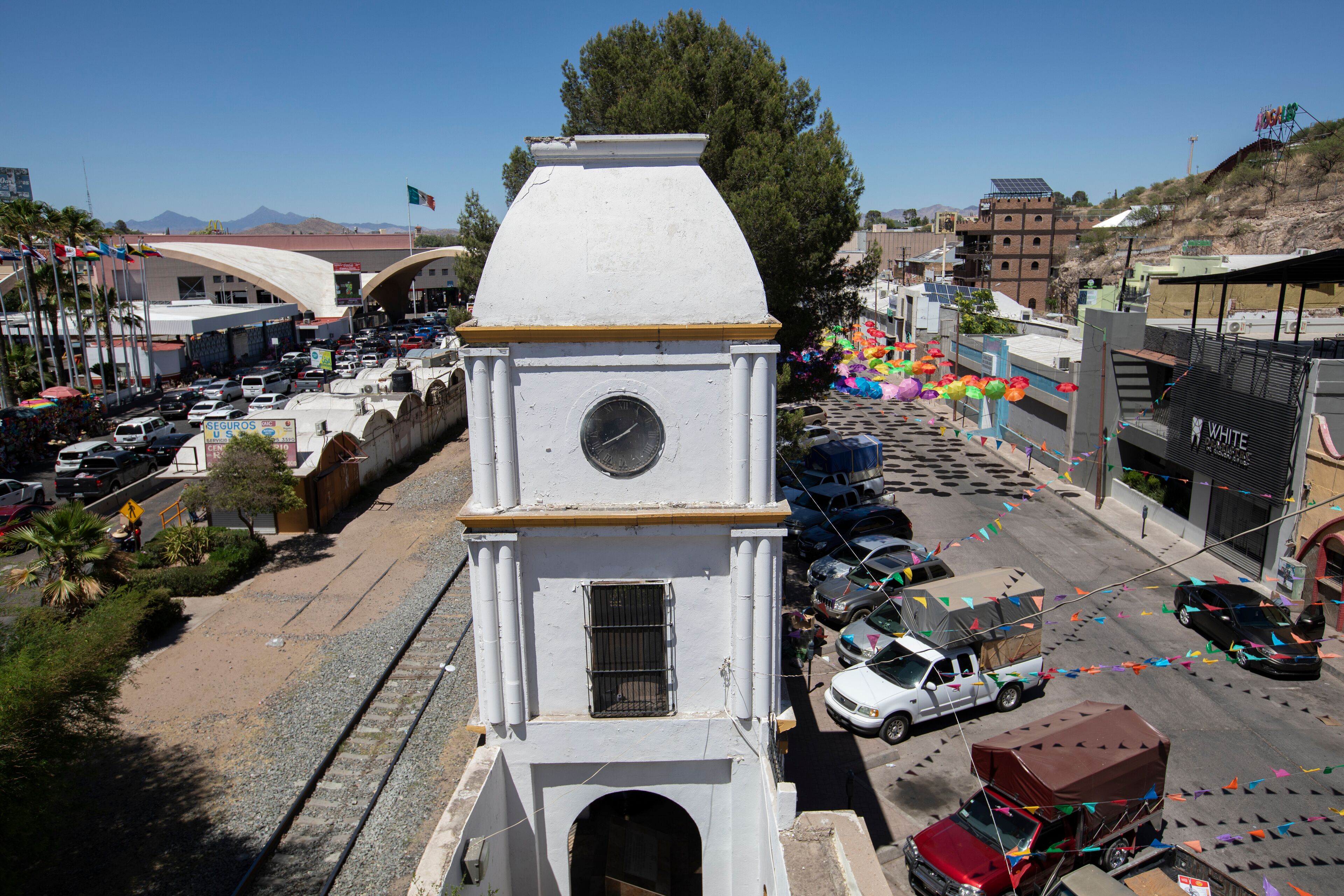 A white clock tower with a round dial, surrounded by a busy street with cars and colorful decorations.