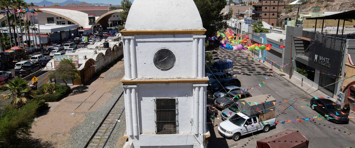 A white clock tower with a round dial, surrounded by a busy street with cars and colorful decorations.