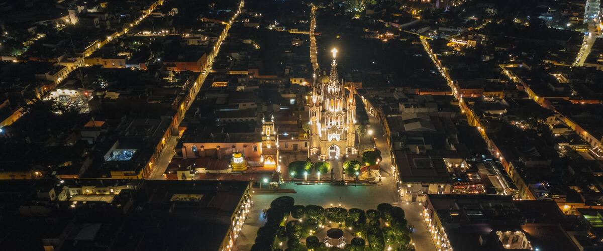 the church Parroquia Archangel Jardin Town Square Night Tree Decoraciones San Miguel de Allende, México. Parroaquia. Night and morning light in a drone view.