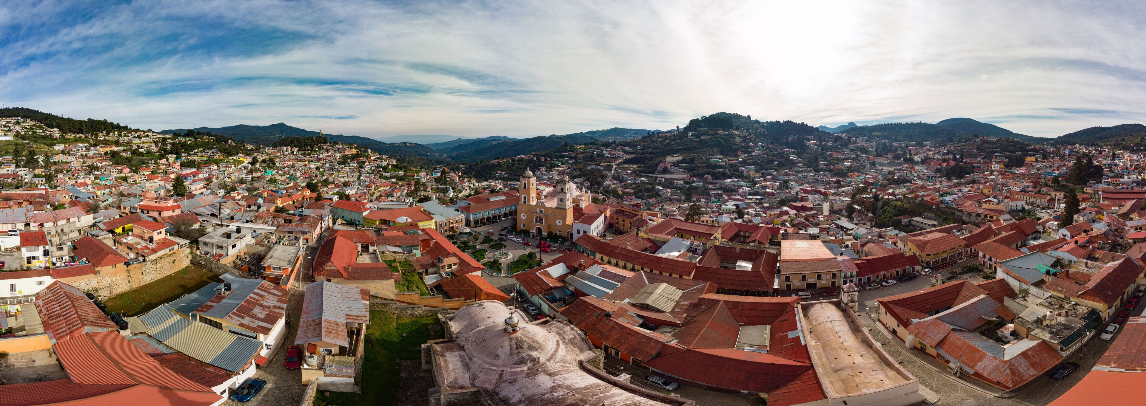 A panoramic view of a historic town with red-roofed buildings, a prominent church, and surrounding hills.