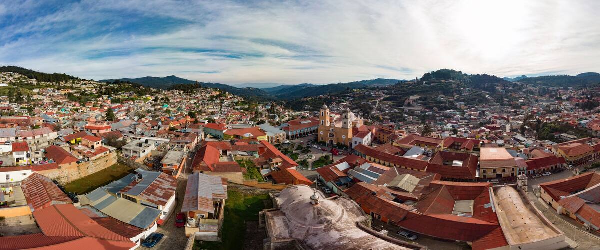A panoramic view of a historic town with red-roofed buildings, a prominent church, and surrounding hills.