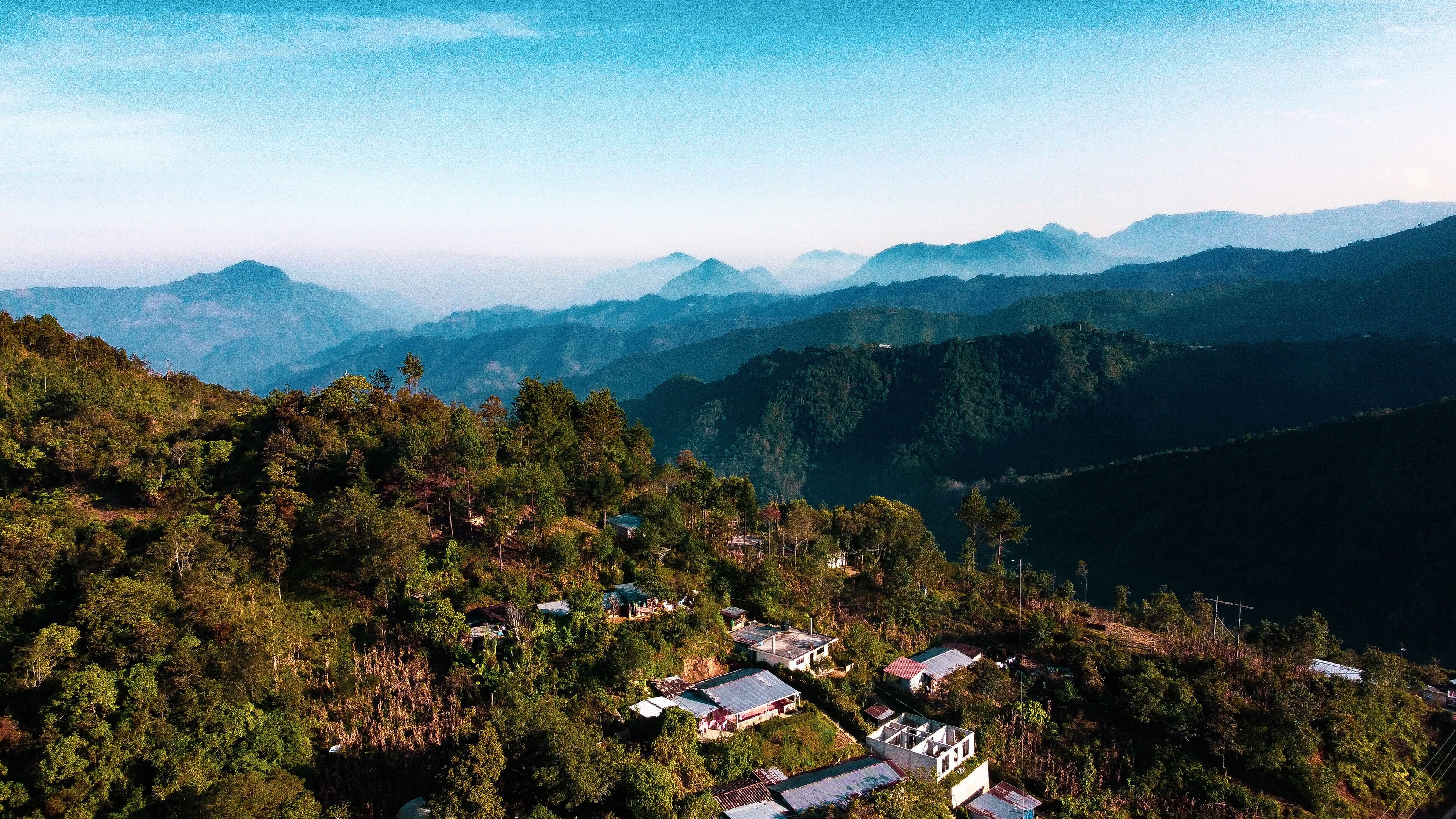 A mountainous landscape with scattered houses amidst dense forests.