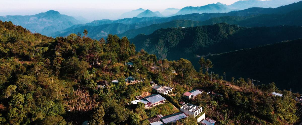 A mountainous landscape with scattered houses amidst dense forests.