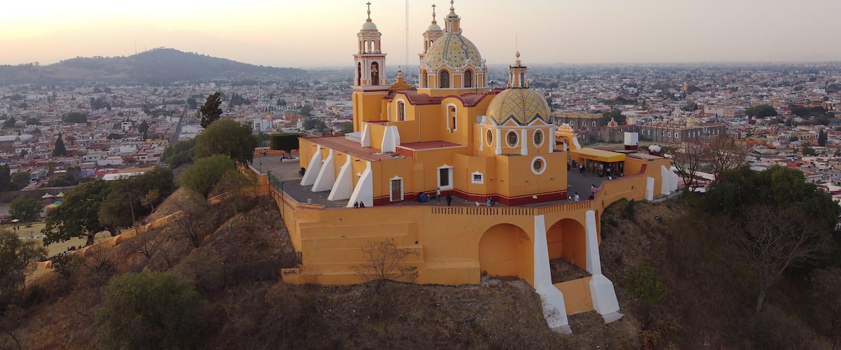 A large yellow church with two towers and a dome, surrounded by a cityscape and hills.