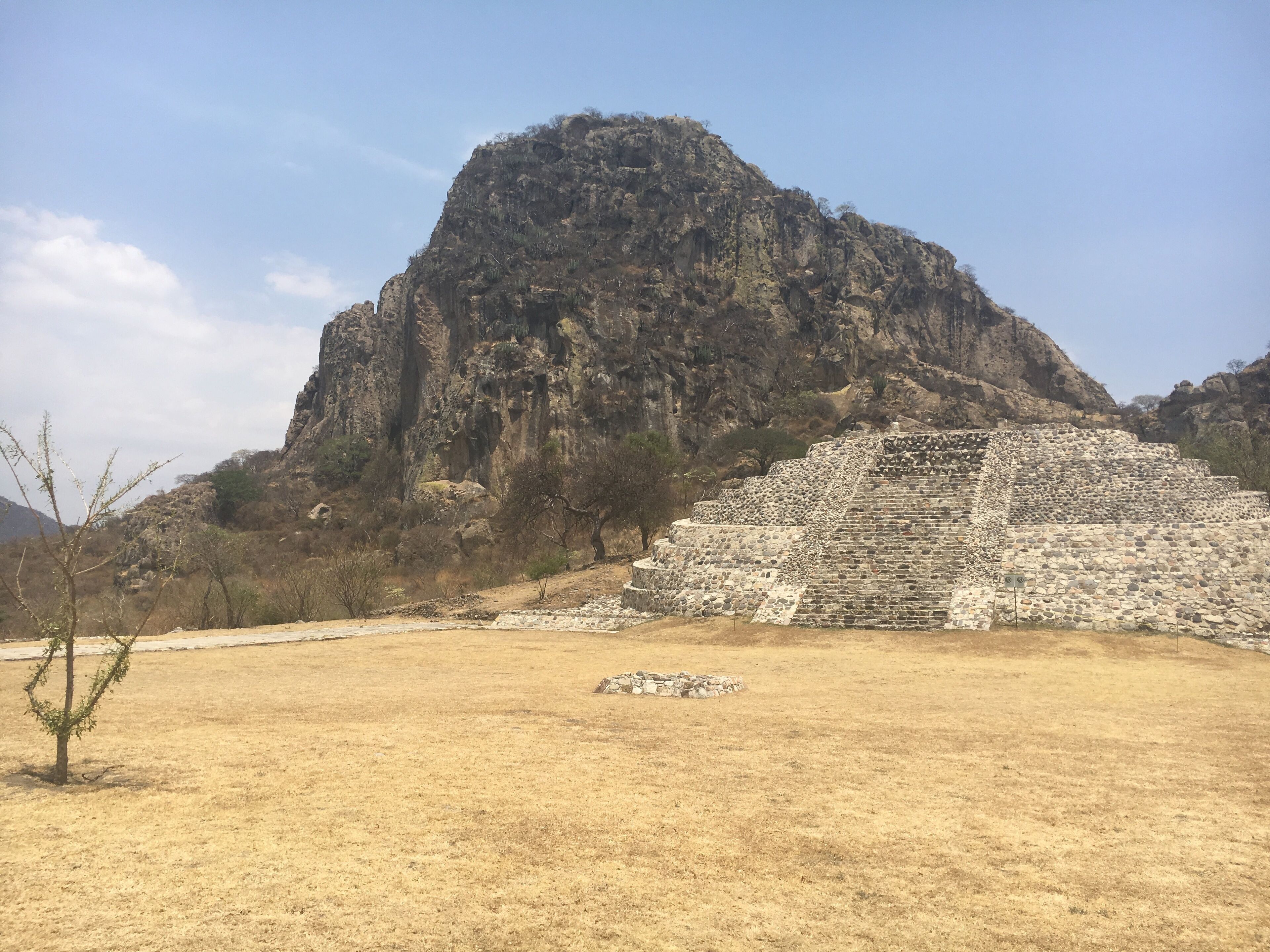 A pyramid structure in a dry, grassy field with a rocky mountain in the background.