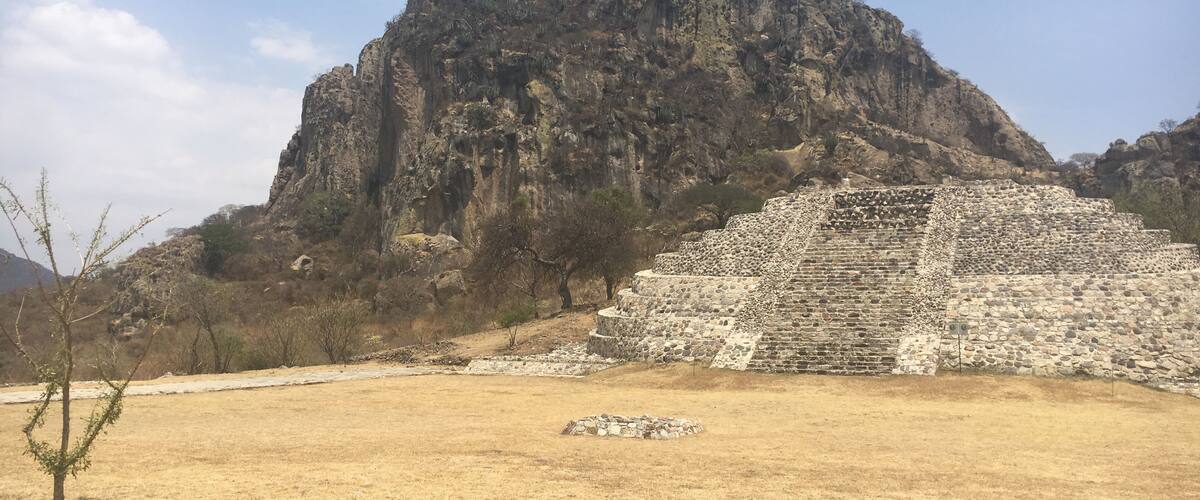 A pyramid structure in a dry, grassy field with a rocky mountain in the background.