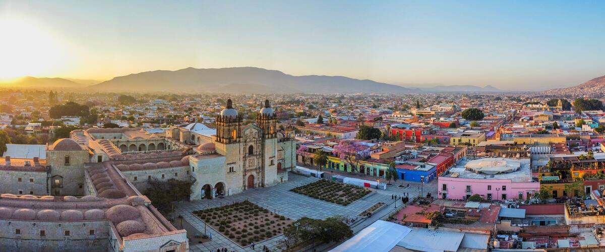 A historic cityscape with a prominent cathedral, a large open square, and a mountainous backdrop.