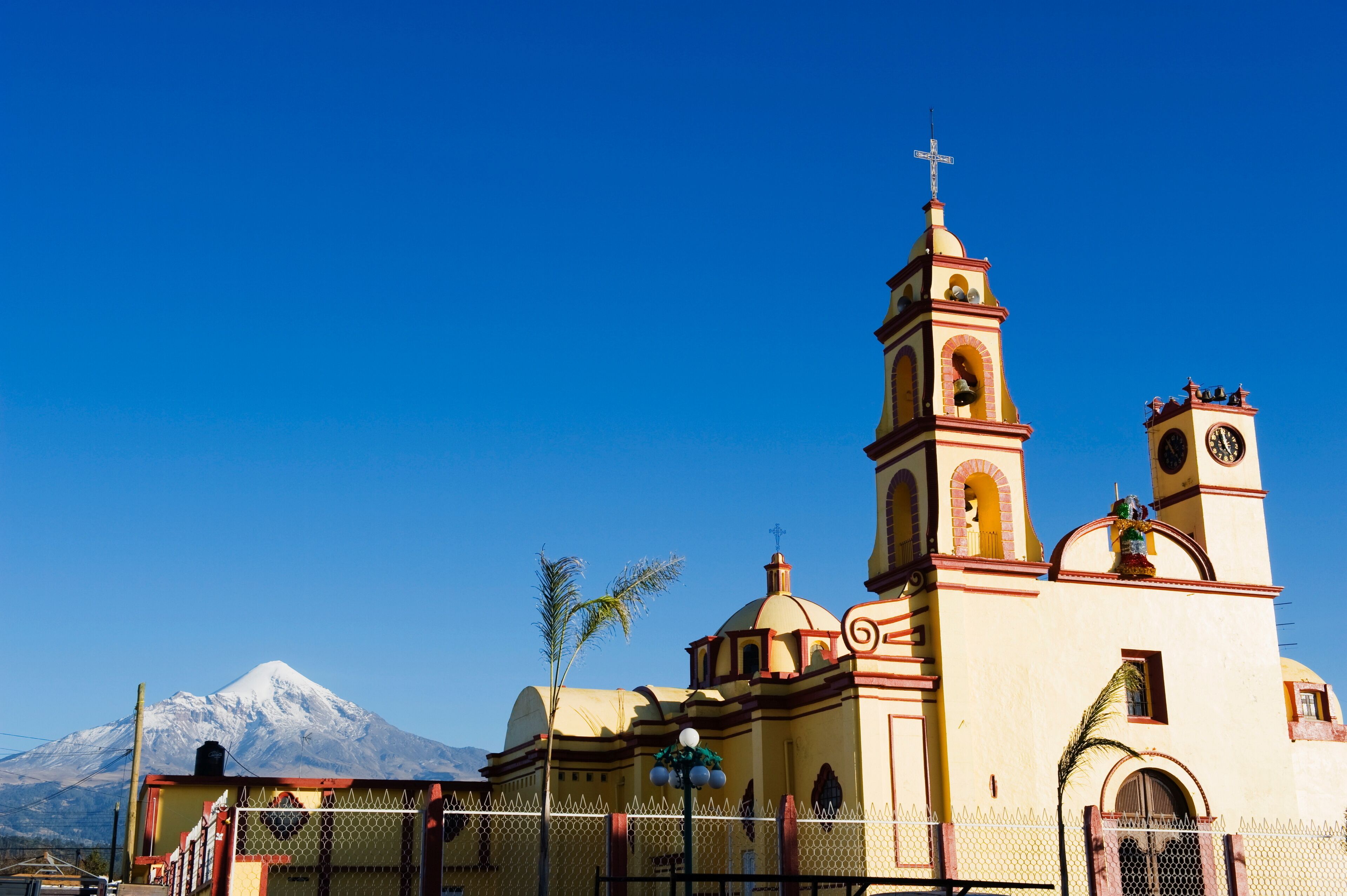 A church with a bell tower and a snow-capped mountain in the background.