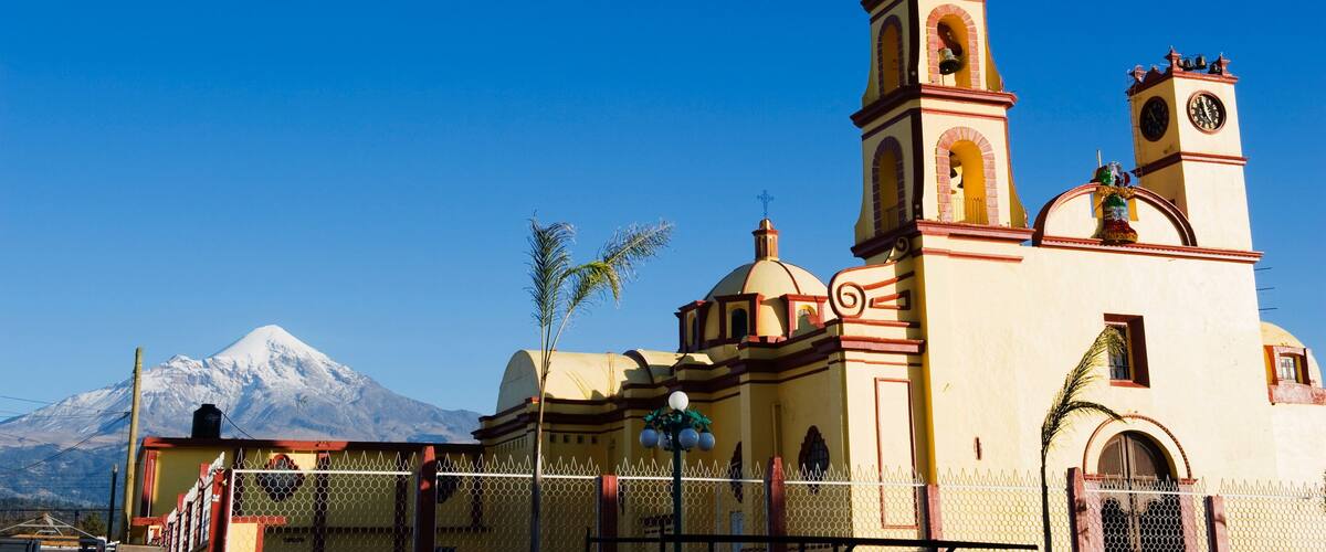 A church with a bell tower and a snow-capped mountain in the background.
