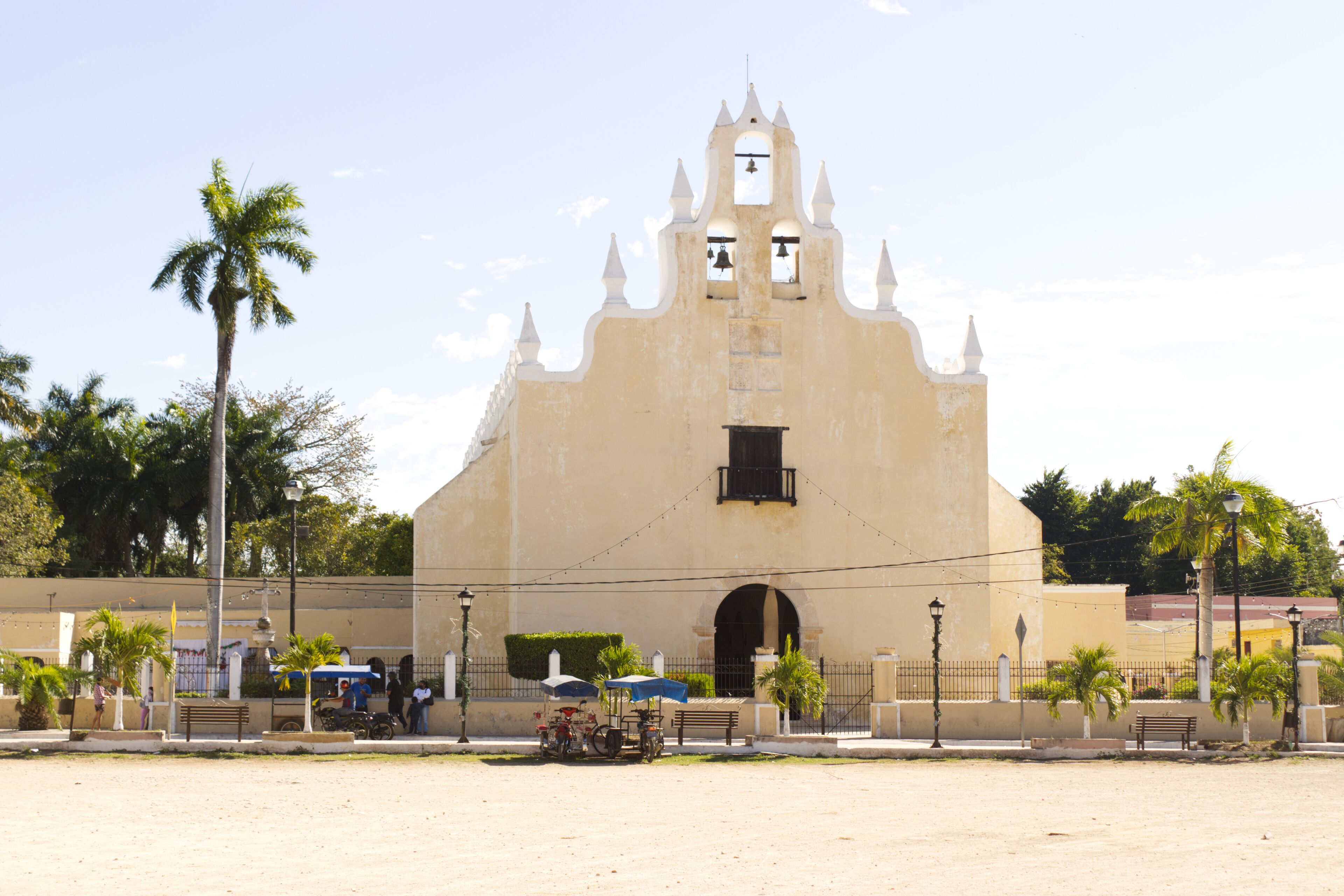 A colonial-style building with a bell tower, palm trees, and a paved plaza.