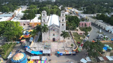 Una iglesia blanca grande con un campanario, rodeada de puestos de mercado coloridos y palmeras.