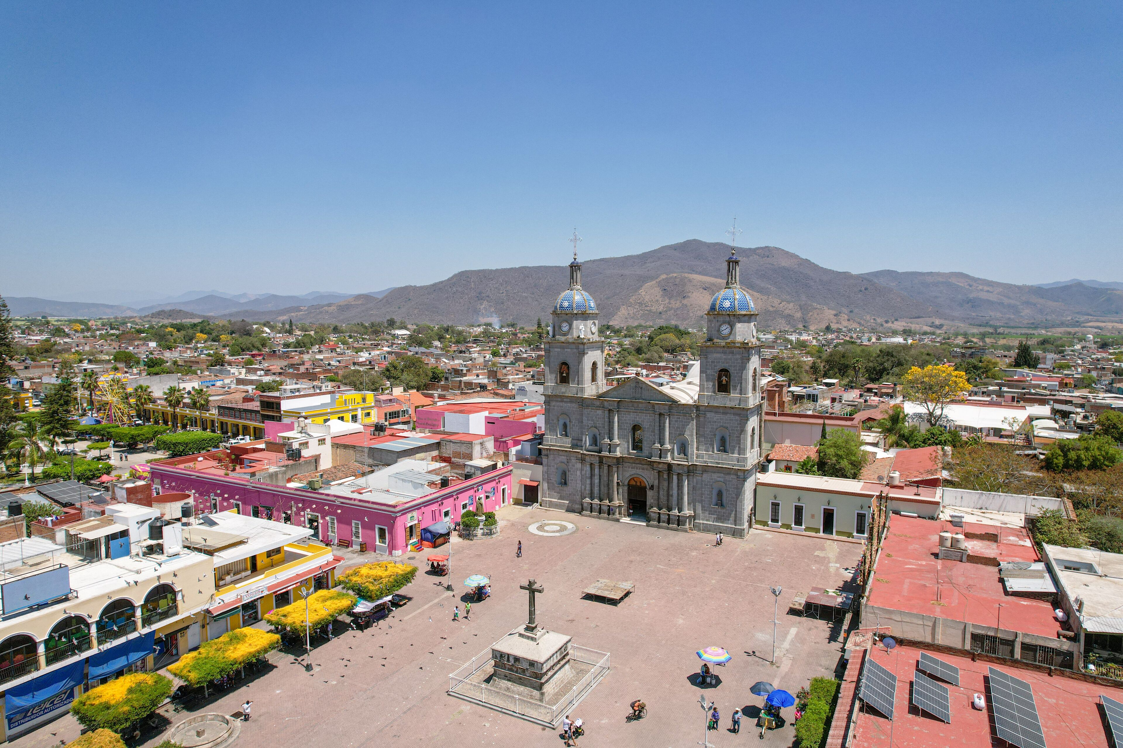 A plaza with a church, colorful buildings, and mountains in the background.