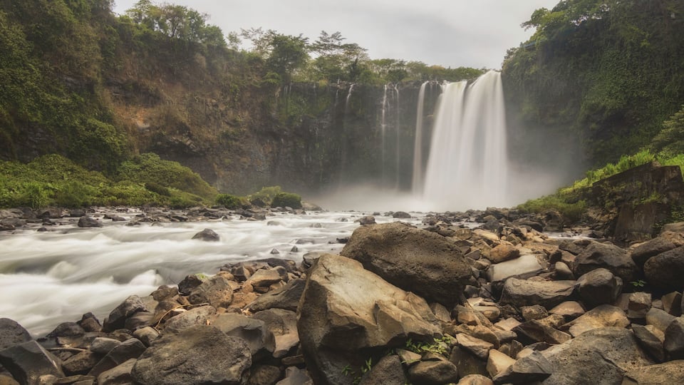 A waterfall cascading over rocks, surrounded by lush greenery.