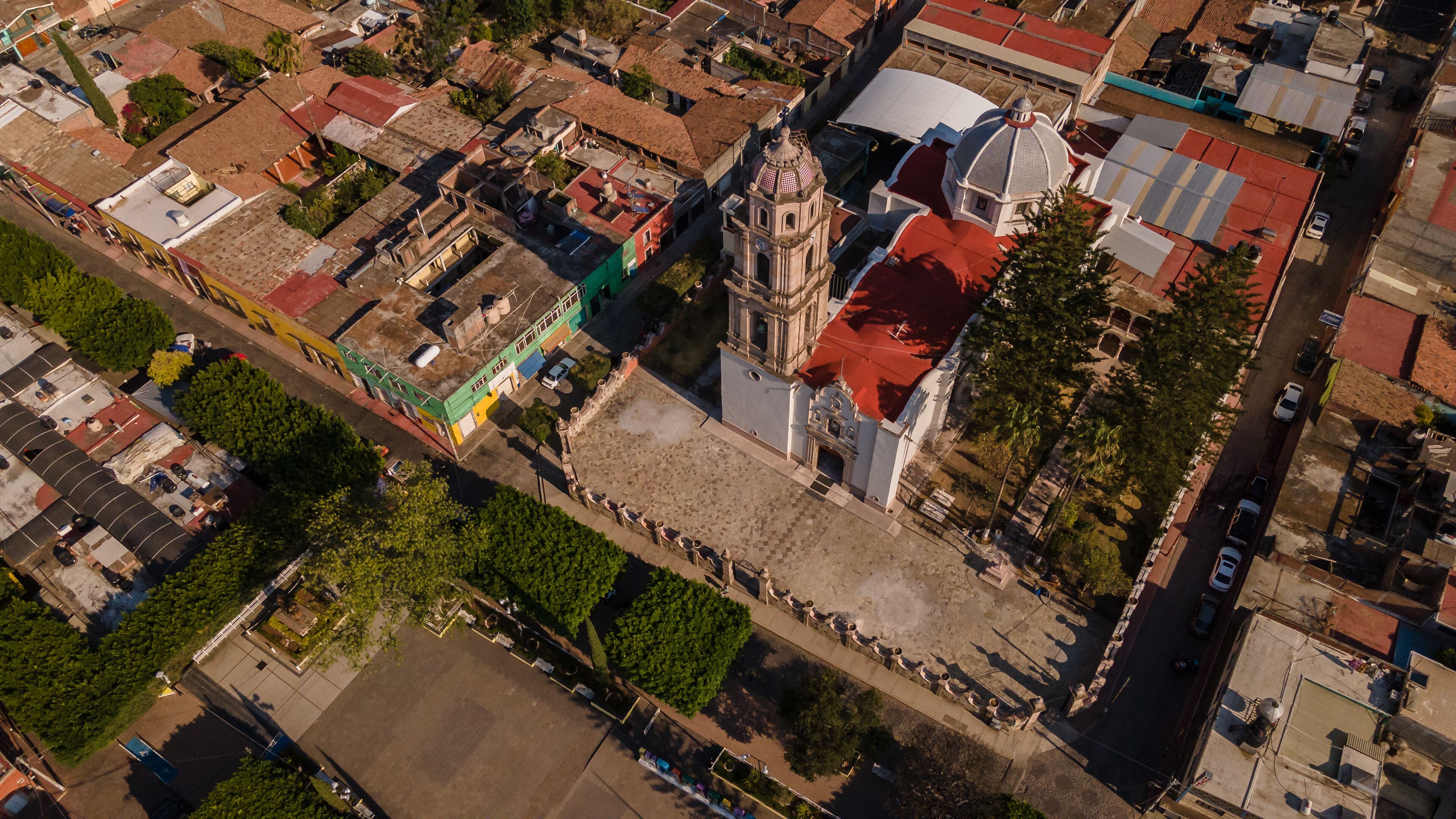An aerial view of a city with a prominent church with a bell tower, surrounded by residential buildings and a large open plaza.