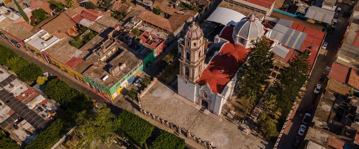 An aerial view of a city with a prominent church with a bell tower, surrounded by residential buildings and a large open plaza.