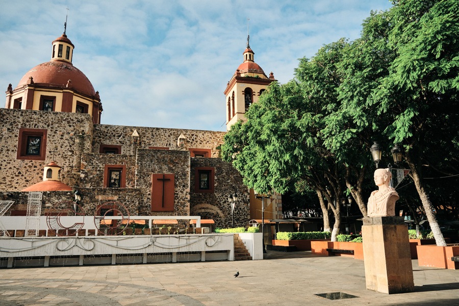 A historic building with two domed towers, a stone facade, and a statue in the foreground.