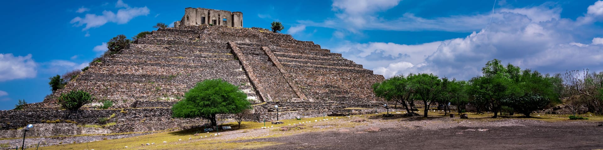 A large pyramid with a smaller structure on top, surrounded by trees and a clear blue sky.