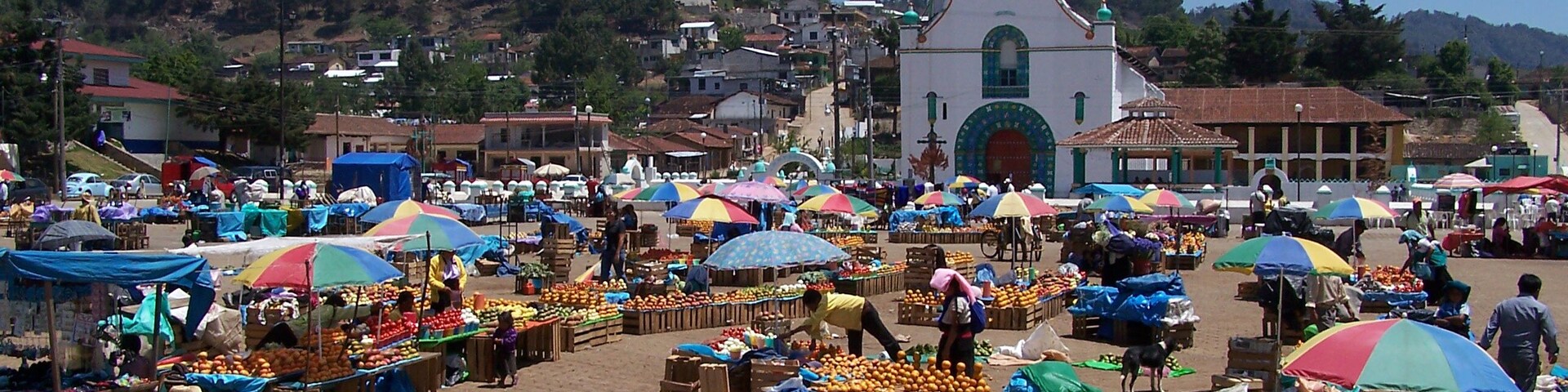 Un mercado al aire libre animado, con sombrillas de colores y vendedores ofreciendo frutas y verduras.