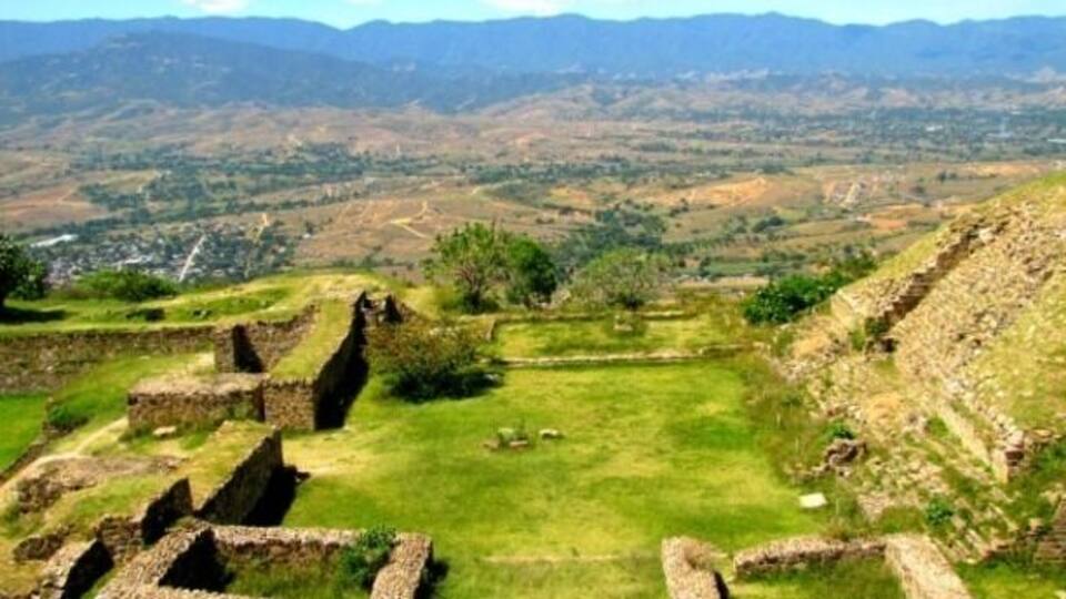Des ruines antiques, avec des murs de pierre et un champ verdoyant, se dressent sur un paysage montagneux.