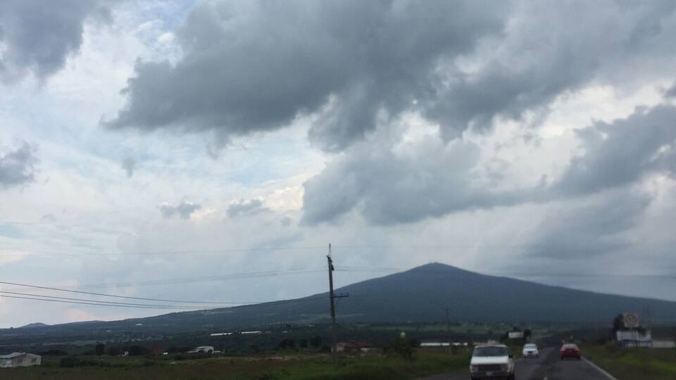 A road with vehicles, a mountain in the distance, and cloudy skies.