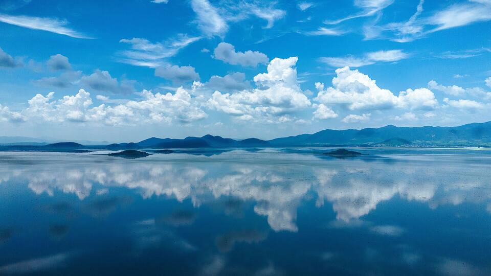 Mirror-like reflections on Lake Cuitzeo, Michoacán: A serene fusion of blue sky, puffy clouds, and water, crafting a captivating two-dimensional illusion