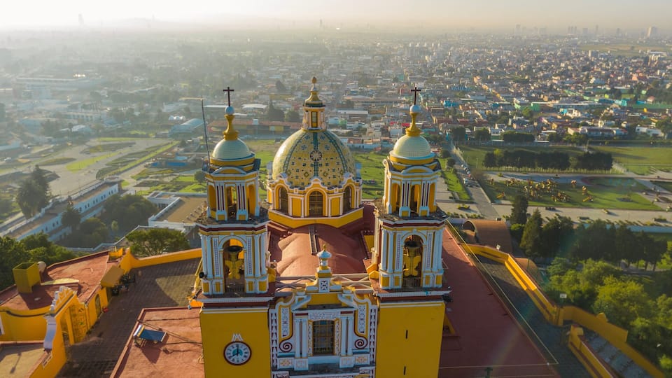 A large yellow church with two towers and a dome, surrounded by a cityscape.