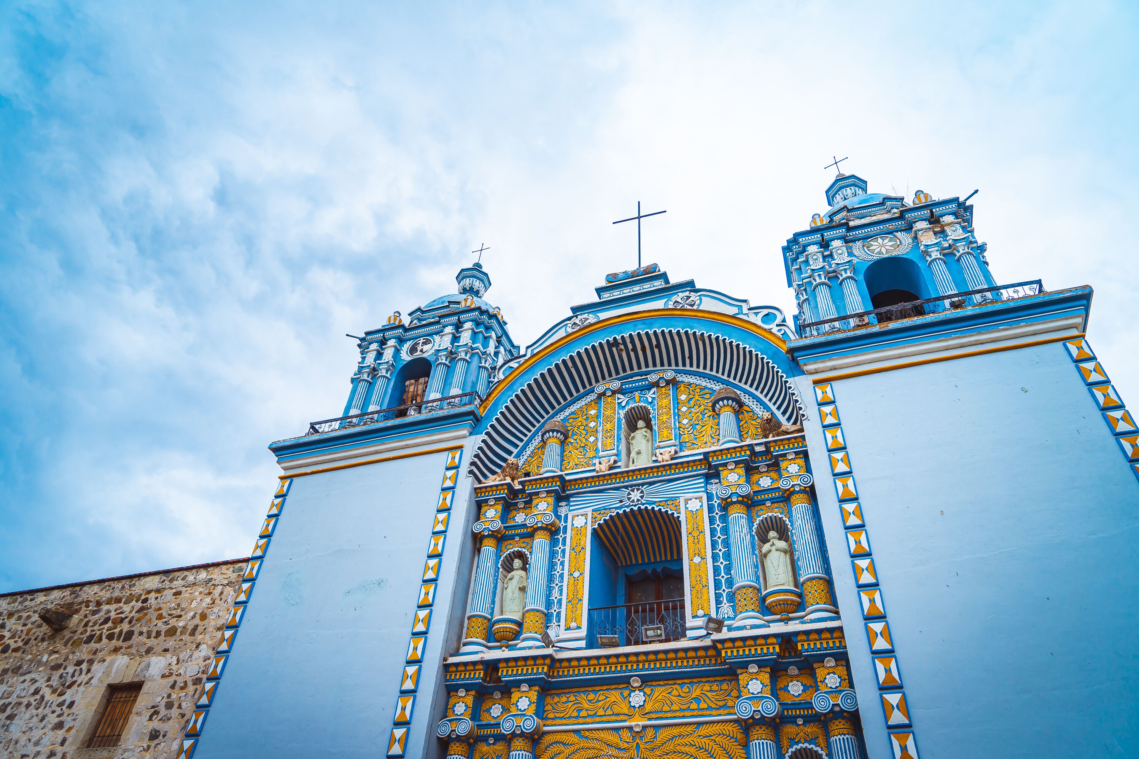 A church with blue and yellow ornate architecture, two bell towers, and a cross on top.
